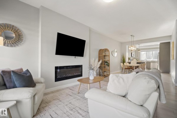 Living room featuring a fireplace, mounted TV, light wood furniture, and a view of the dining area and kitchen. - 7437 Creighton Pl Sw, Edmonton