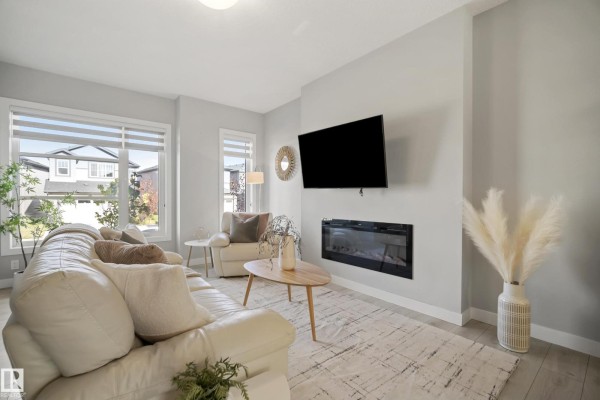 Bright living room with a large sectional couch, coffee table, fireplace, and windows overlooking the street. - 7437 Creighton Pl Sw, Edmonton