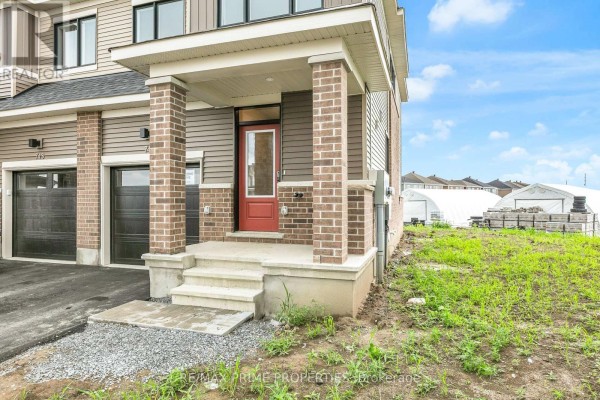Front entrance of a townhouse with beige siding, brick accents, and a red door. - 745 Haflinger Row, Ottawa