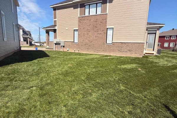 Side view of a townhouse showing beige siding, brick accents, and an unfinished lawn. - 745 Haflinger Row, Ottawa