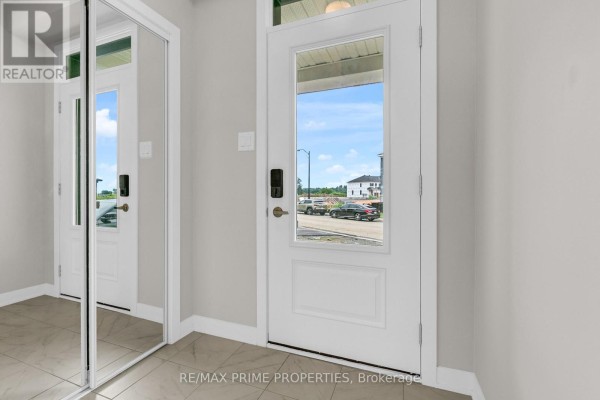 Rear exterior of a townhouse with beige siding, brick accents, and a back door. - 745 Haflinger Row, Ottawa