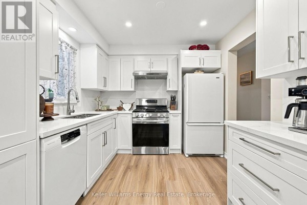 Modern white kitchen with stainless steel appliances and light wood laminate flooring. - 746 Elderberry Drive, Oshawa