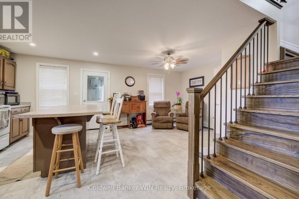 Open concept living area with a kitchen island, island stools, recliner chairs, and a staircase. - 748 Arthur Street, West Grey