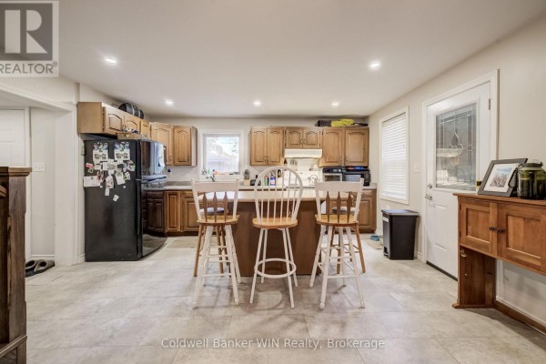 Kitchen with wooden cabinets, a refrigerator, an island with stools, and a doorway to outside. - 748 Arthur Street, West Grey