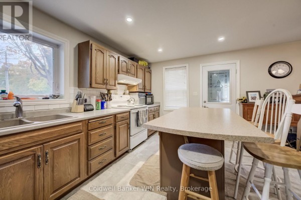 Kitchen counter space with sink, wooden cabinets, a white stove, and an island with stools. - 748 Arthur Street, West Grey