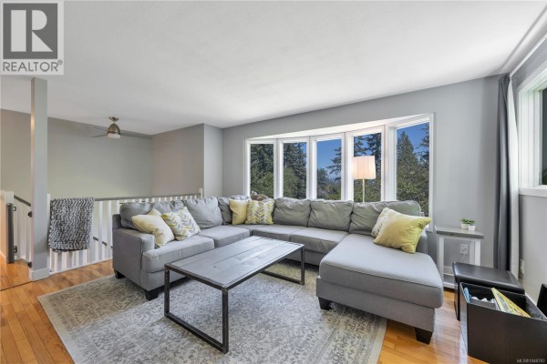 Bedroom with a king-size bed, bay window with blue curtains, and a wooden floor. - 7487 Forest Turn Way, Lantzville