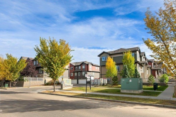 Street view of townhouses with colorful exteriors and green lawn under a blue sky. - #75 3305 Orchards Link Li Sw, Edmonton