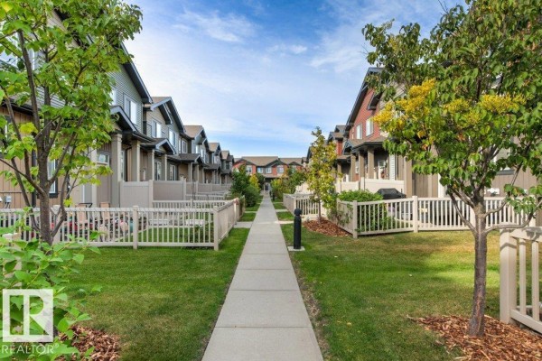 Pathway between identical townhouses with white picket fences and manicured lawns. - #75 3305 Orchards Link Li Sw, Edmonton