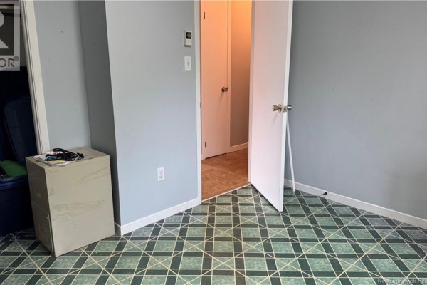 Small room with grey walls, patterned green floor tiles, and a light beige filing cabinet. - 75-77 Belisle Street, Edmundston