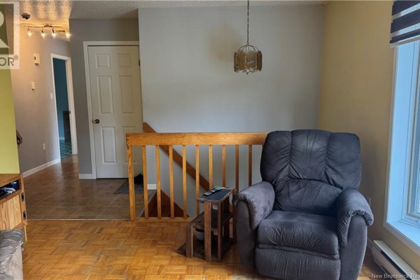 Living room with a recliner, wooden railings for stairs, and a view of the entrance hallway. - 75-77 Belisle Street, Edmundston
