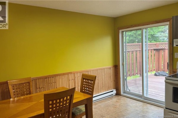 Dining area with a wooden table and chairs, lime green walls, wood paneling, and sliding glass doors. - 75-77 Belisle Street, Edmundston