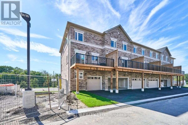 Rear exterior view of townhouse complex with multiple garages and wooden balconies. - 75 Addyman Crescent, Clarington