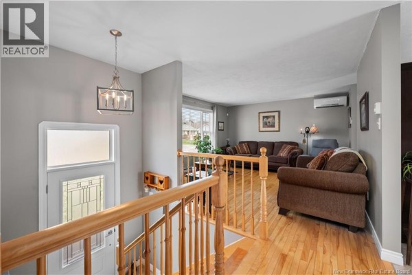 Interior view of a hallway with wood railings, gray walls, and a view into a living room with brown furniture. - 75 Anik, Dieppe