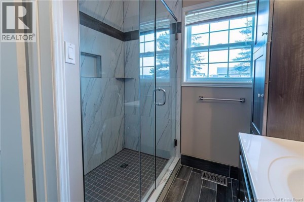 Modern bathroom with a glass-enclosed tiled shower stall, vanity, and a window with blinds. - 75 Delaney Street, Grand Sault/grand Falls