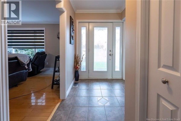 Interior view of a tiled foyer with double glass front doors, leading to a living room with hardwood floors. - 75 Delaney Street, Grand Sault/grand Falls