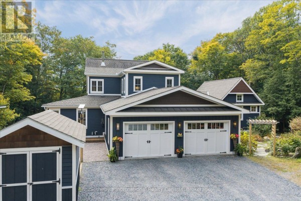 Front view of a dark blue house with a grey roof and a three-car garage in autumn. - 75 Dora Creek Lane, Seguin