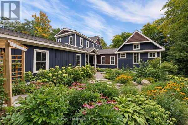 Side view of a dark blue house with wood accents and a garden with pink and yellow flowers. - 75 Dora Creek Lane, Seguin