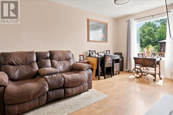 Living room with a brown leather reclining sofa, light wood laminate flooring, and a large window overlooking trees. - 75 Edison Crescent, Stratford