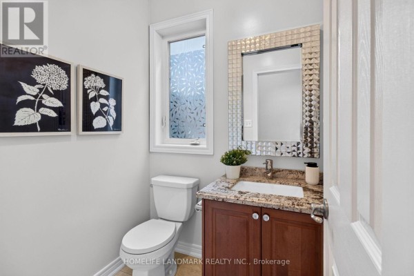 Powder room with a white toilet, a granite-topped vanity with a dark wood cabinet, and a decorative mirror. - 75 Estrella Crescent, Richmond Hill