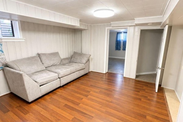 Living area with grey sofa, wood-look flooring, and a window. - 75 Kootenay Crescent, Toronto