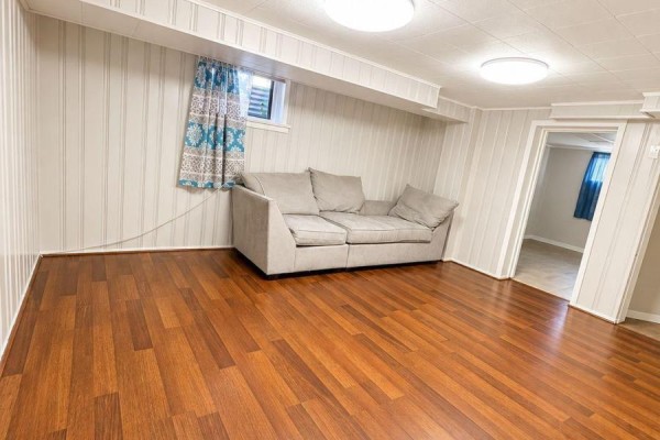 Basement living space with sectional sofa, wood flooring, and two doorways. - 75 Kootenay Crescent, Toronto