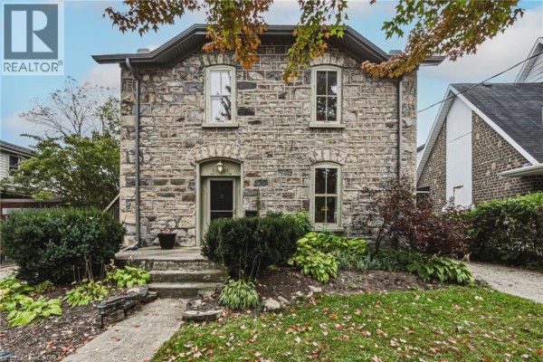 Front exterior of a historic stone house with arched doorway, dual-pane windows, and neat landscaping. - 75 Pollock Avenue, Cambridge