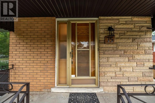 Close-up of the front entrance with a brick wall, stone facade, and a double glass door. - 75 Purdy Crescent, Hamilton