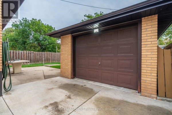 Side view of the detached garage with a brown door, surrounded by concrete. - 75 Purdy Crescent, Hamilton