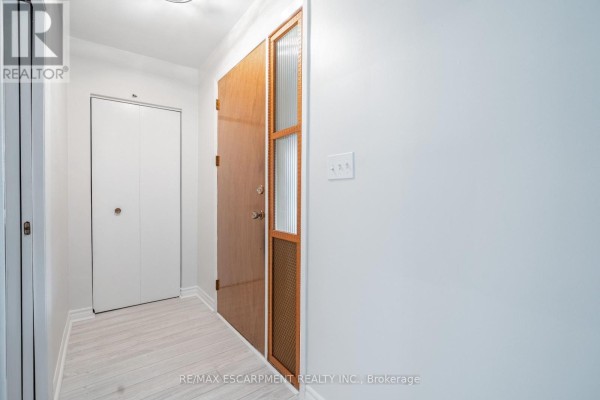 Interior view of a hallway with light grey wood-look flooring and a closed white double door. - 75 Purdy Crescent, Hamilton