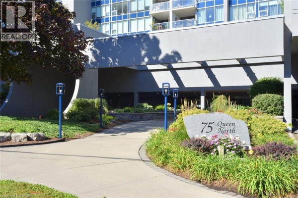 An entrance walkway leads to the building's overhang, past landscaping and a stone address marker. - 75 Queen Street N Unit# 2007, Hamilton