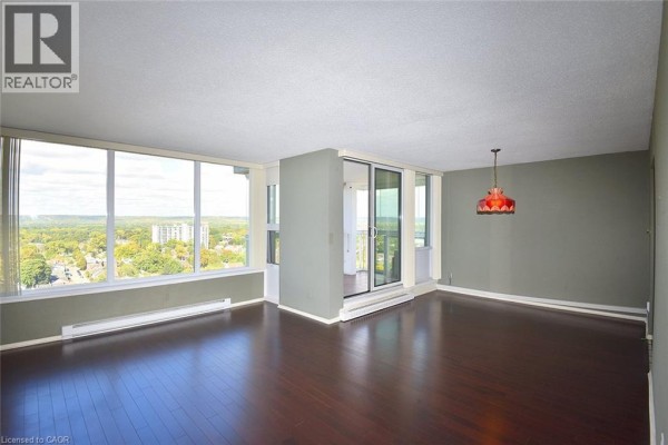 Living room with dark wood floors, large windows, and a glass door leading to a balcony. - 75 Queen Street N Unit# 2007, Hamilton