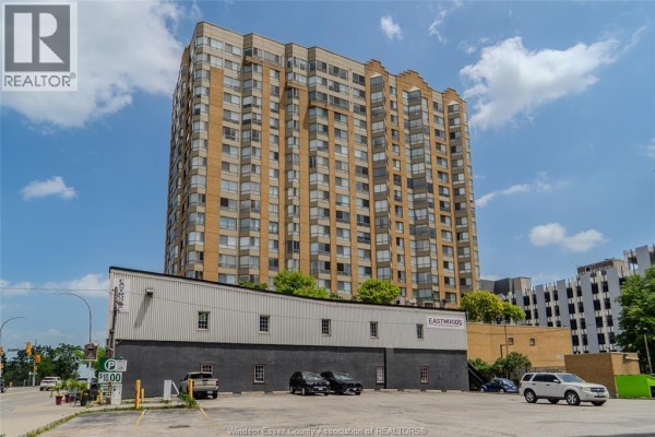 Rear exterior view of a beige high-rise apartment building with parking lot. - 75 Riverside Drive East Unit# 1609, Windsor