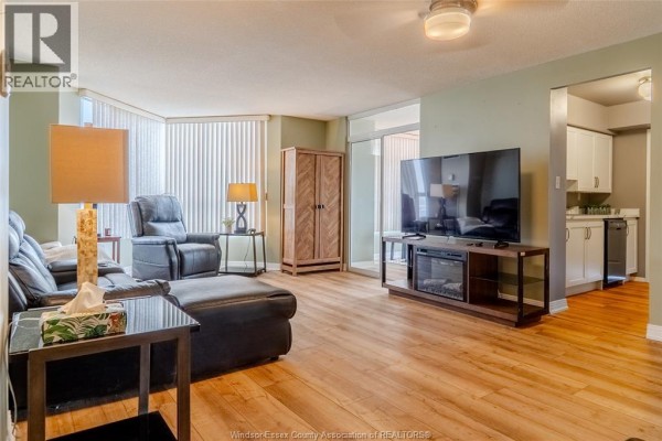 Living room with a black leather sectional sofa, recliner, entertainment unit, and wood floor. - 75 Riverside Drive East Unit# 1609, Windsor