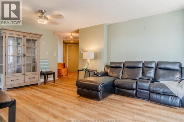 Living room with a black leather sectional, a dresser, and wood floor. - 75 Riverside Drive East Unit# 1609, Windsor