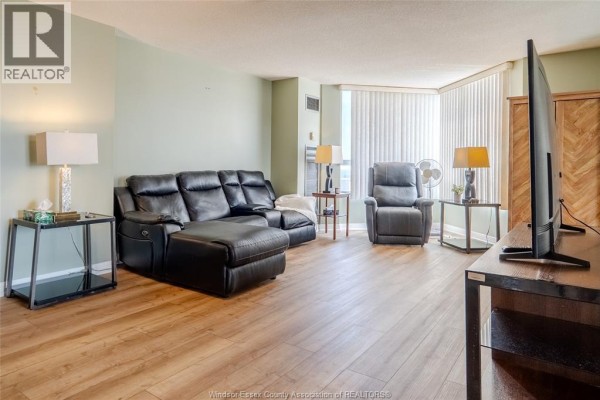 Living room with black leather furniture, a dresser, and large windows with blinds. - 75 Riverside Drive East Unit# 1609, Windsor