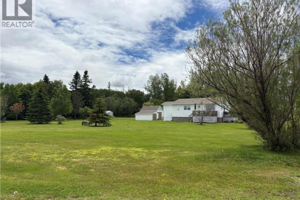 Distant view of white bungalow and detached garage set on a large, grassy lot with trees. - 75 Rue Des Chalets, Pointe Verte