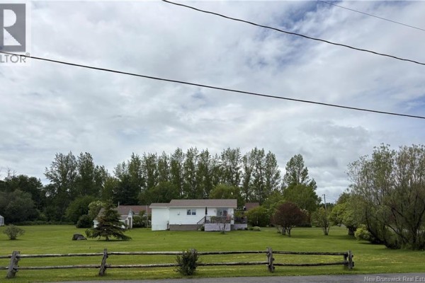 Wide shot of white house and outbuildings with a split wooden fence in the foreground and trees behind. - 75 Rue Des Chalets, Pointe Verte
