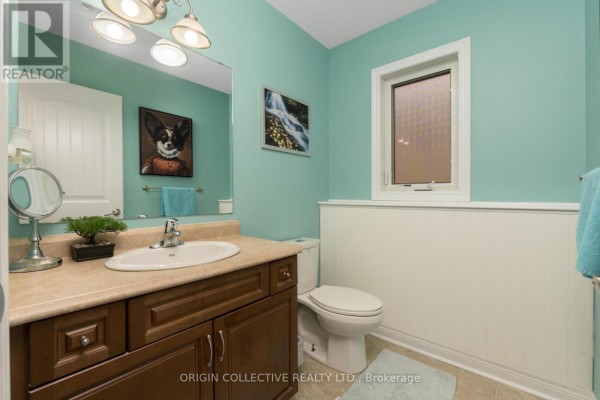 Bathroom with aqua walls, wainscoting, a dark wood vanity, white toilet, and a small window. - 75 Sheffield Street, Southgate