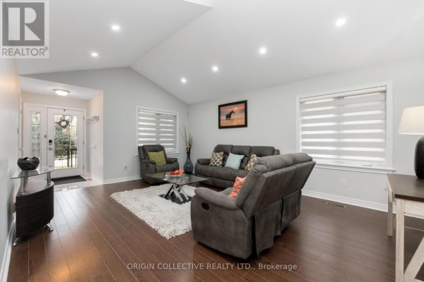 Living room with vaulted ceiling, hardwood floors, gray sofas, a glass coffee table, and two large windows. - 75 Sheffield Street, Southgate