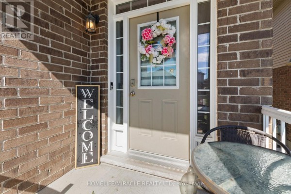 Covered front porch with brick exterior, beige door, wreath, and a welcome sign. - 75 Sparrow Avenue, Cambridge