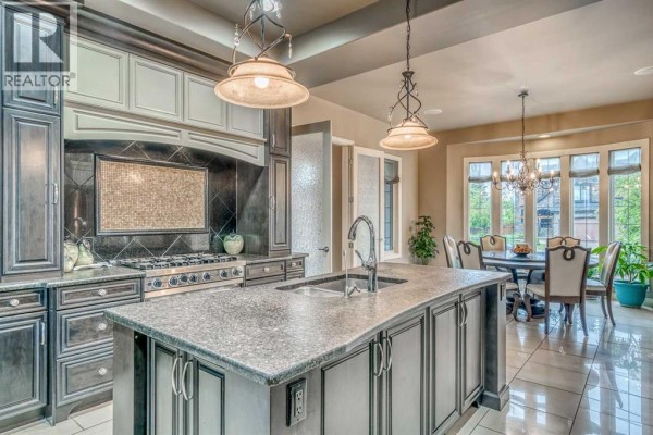 Kitchen with a gas range, granite island, and a view of the adjacent dining area with a chandelier. - 75 Wentworth Terrace Sw, Calgary