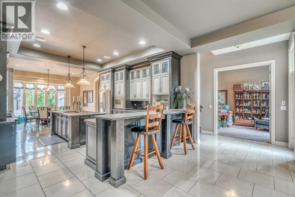 View of a kitchen island with bar seating, opening into a dining area and a den with shelves. - 75 Wentworth Terrace Sw, Calgary