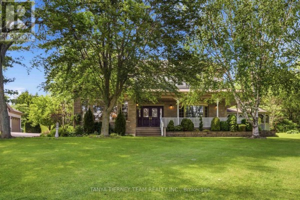 Front view of the residence featuring a covered porch, stone accents, double dark wood doors, and lush landscaping. - 75 Woodbridge Circle, Scugog
