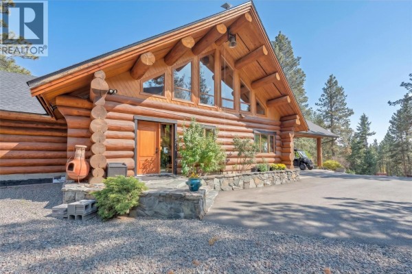Side view of a log home with a stone foundation and entrance, surrounded by landscaping and trees. - 750 Cedar Creek Road, Princeton