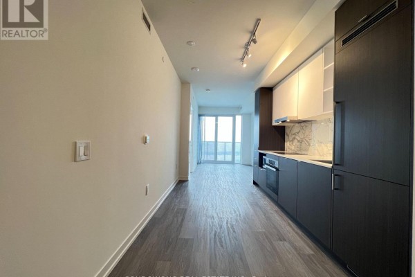 View of the kitchen and living area from the entryway, featuring dark and white cabinetry and wood flooring. - 7510 - 55 Cooper Street, Toronto