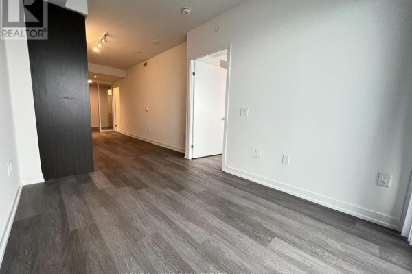 View down the hallway from the living area, with white walls and doors, and dark wood flooring. - 7510 - 55 Cooper Street, Toronto