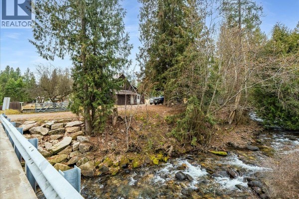 Stream flowing past a log cabin surrounded by trees and gravel. - 7515 Broadwater Road, Deer Park