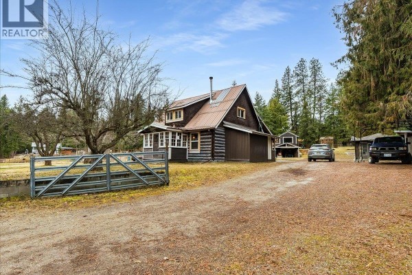 Log cabin exterior with a gravel driveway and parked vehicles. - 7515 Broadwater Road, Deer Park