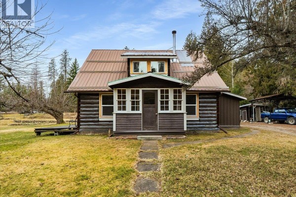 Front view of log cabin with a metal roof and landscaped yard. - 7515 Broadwater Road, Deer Park