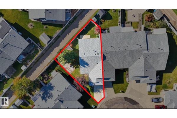 Side angle of the townhouse exterior showing the entrance, garage, and manicured lawn. - 7527 138a Av Nw, Edmonton